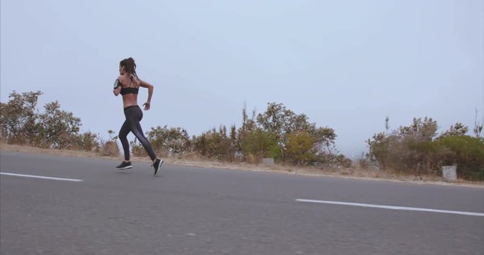 Outdoor shot of fitness woman running on open country road in morning. Female athlete on outdoor training session.
