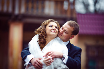 Groom hugs a curly bride from behind standing in the front of a