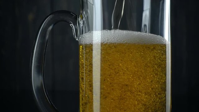 Slow motion shot of pouring beer into beer mug. Over dark wooden background