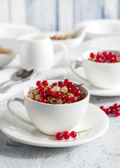Two white cups with red currant. Light blue background. Breakfast.