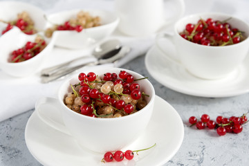 Two white cups with red currant. Light blue background. Horizontal photo.