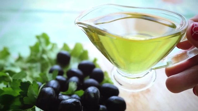 Slow motion of pouring olive oil from glass bottle among olives
