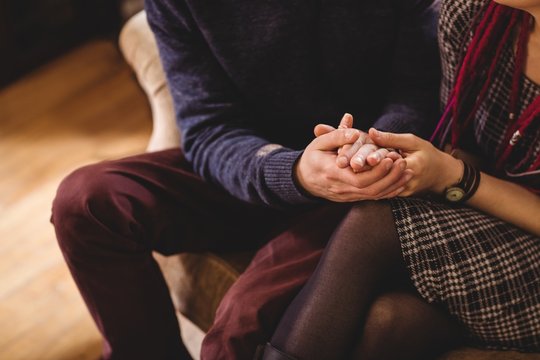 Midsection of couple holding hands while sitting on sofa