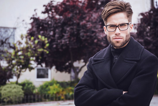 Young handsome trendy man with coat posing with trees background