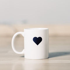 White breakfast mug isolated on a wooden table with a heart painted on it