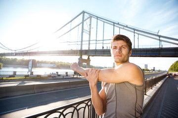 Sports man stretching at the bridge railing and looking away