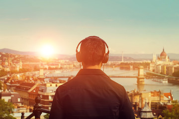 Young man listening music in sunset back view with Budapest