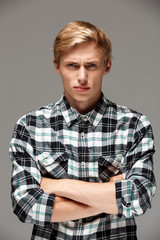 Angry blond handsome young man wearing casual plaid shirt with hands crossed on chest looking at camera, copy space, grey background