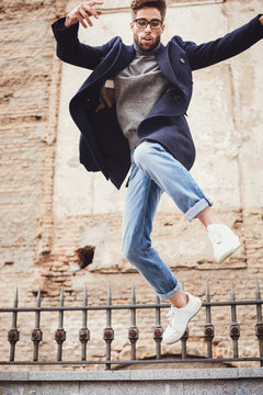 Young handsome trendy man with coat jumping with an old wall bac
