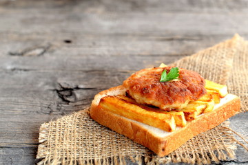 Sandwich with fried potatoes and meat cutlet on a burlap and on old wooden table for empty space for text. A sandwich cooked from slice of white bread, fried potatoes and Turkey cutlet