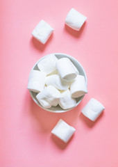 Marshmallow in a white bowl on a pink background, top view