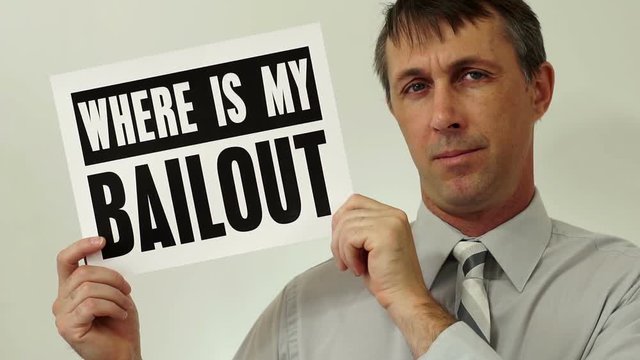 Middle aged man wearing a dress shirt and tie holds up a sign that asks where his bailout is which refers to his financial situation and bankruptcy.