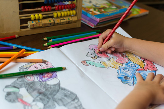 Ребенок разукрашивает рисунок карандашами.