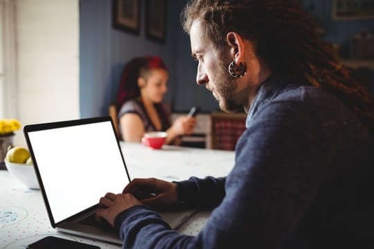 Man using laptop while woman sitting at home