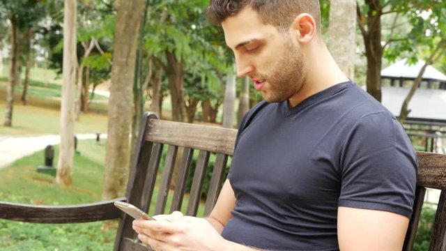Young man sending SMS - texting in the park