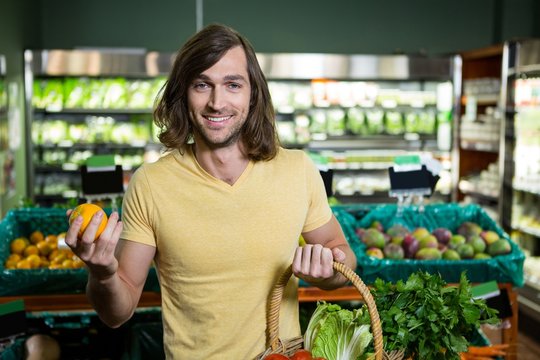 Man holding orange and basket of vegetables