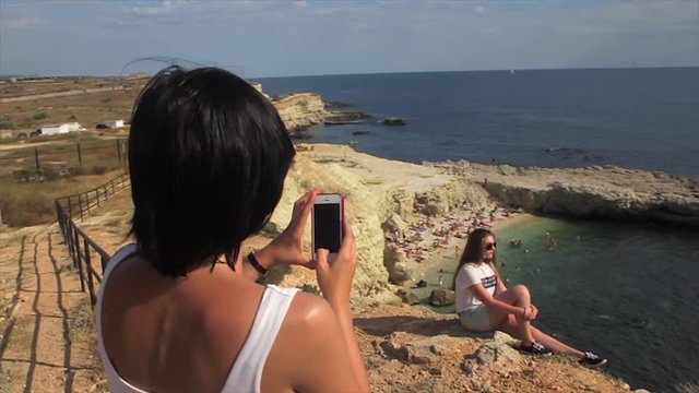 Happy women taking photo friend with smartphone on the background sea lighthouse