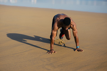 Fit man warming up before running at the beach. Black athlete on hiit cardio outdoor workout. Mountain climbers exercise.