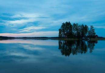 The island in the lake at sunset. The sky in the clouds. The smooth surface of the water.