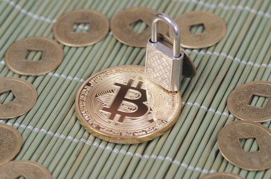 Gold-plated Bitcoin and padlock on a wooden tablecloth. Selective focus.