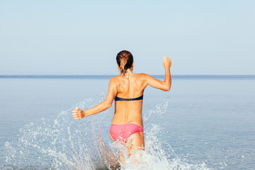 Young woman hight speed running into sea with splashes
