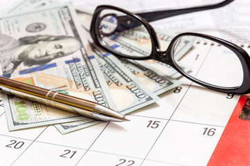Glasses, pen and money on the calendar