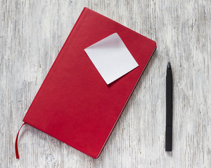 Red notebook with pen on a old white wooden background