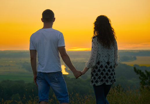 romantic couple looking into the distance at sunset on outdoor, beautiful landscape and bright yellow sky, love tenderness concept, young adult people