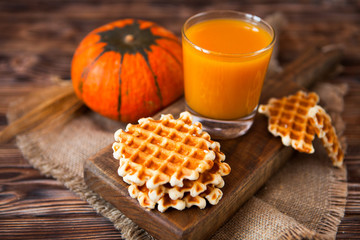 Glass of fresh pumpkin juice with wafer and pumpkin on dark wood