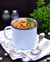 Soup with chickpeas, lentils, rice, beef in a bowl on a black background.