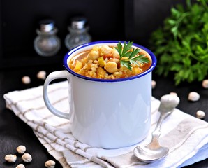 Soup with chickpeas, lentils, rice, beef in a bowl on a black background.