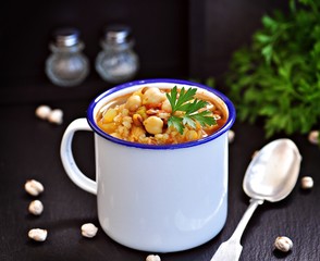 Soup with chickpeas, lentils, rice, beef in a bowl on a black background.