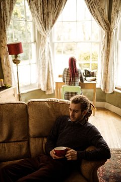 Man with coffee cup while woman in background