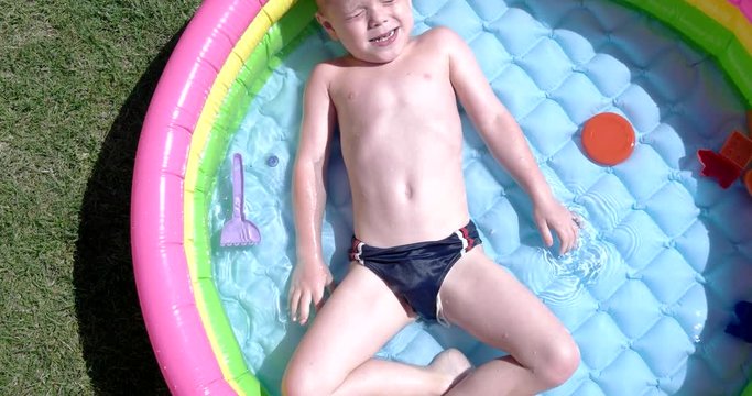 Boy Play and Having Fun in Inflatable Pool on Green Lawn in a Sunny Day