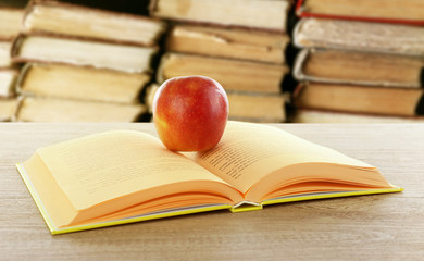 Open book with red apple on blurred library background