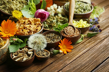 Herb selection and fresh flowers in bowls on wooden background