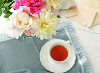 Composition with peony flowers and cup of tea on table closeup