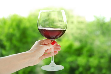 Woman holding glass of wine on blurred natural background