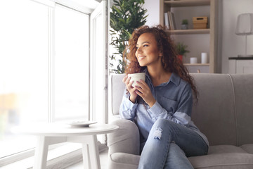 Beautiful African American girl drinking coffee on couch