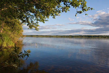 Sunset over the lake in the village. View from the shore in the forest