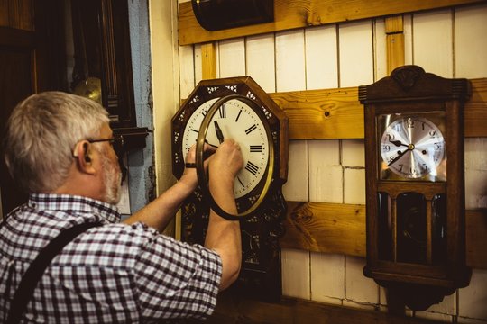 Rear view of horologist repairing a clock hung on wall