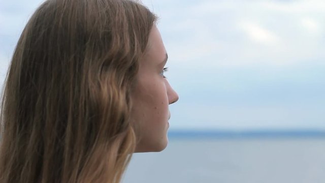 Dreamy teenage girl on beach looking at horizon. Pensive young woman looking at sea. Back view profile close-up portrait