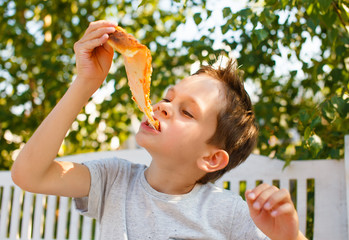 boy eating pizza. child closed his eyes in pleasure and takes a bite of pizza piece holding it aloft