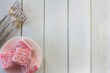 Pink Lamingtons with Forks from Above on White Wooden Table with Copy Space Horizontal