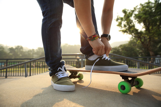 skateboarder tying shoelace at skatepark ramp..
