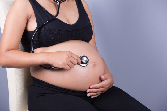 close-up pregnant woman with stethoscope listening belly to baby