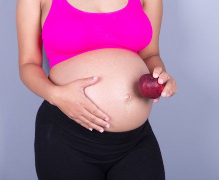 close-up belly of pregnant woman with red apple on gray backgrou