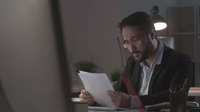 Overwhelmed office worker reading documents and then getting mad at his business mistake. He throwing crumpled paper at table and holding head in hands