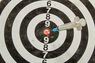 plastic medical syringe stuck in a dartboard closeup