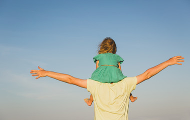 father and little daughter on shoulders play at sky